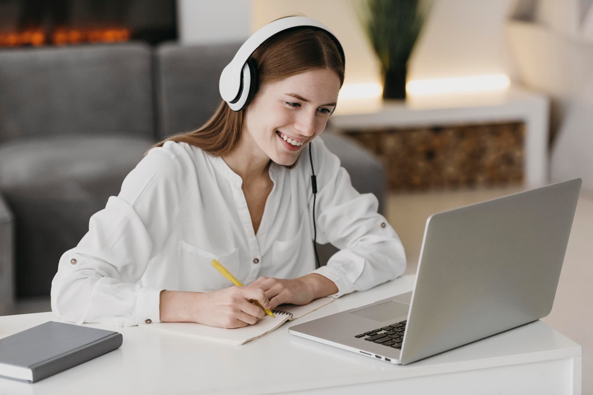 Aluna sorridente assistindo às aulas no notebook e fazendo anotações